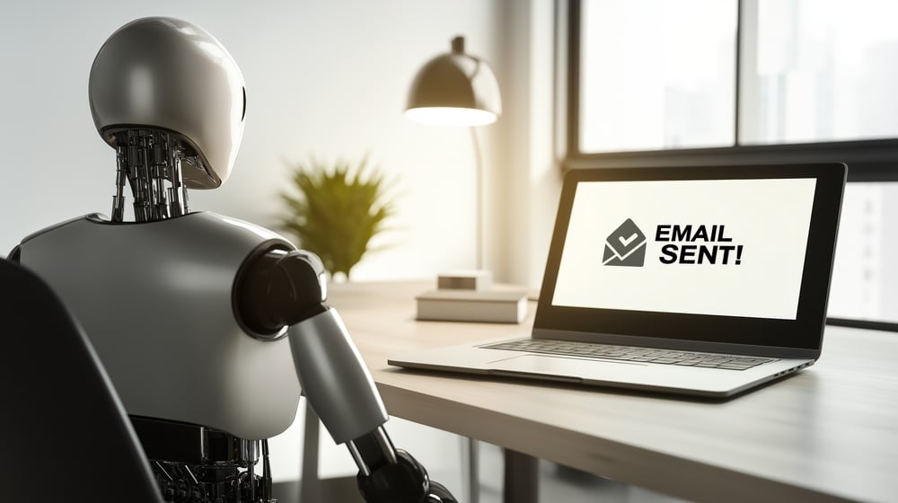 Ein humanoider KI-Agentenroboter, der eine E-Mail auf einem Laptop-Computer versendet, symbolisiert die Handlungsautonomie des Agenten.