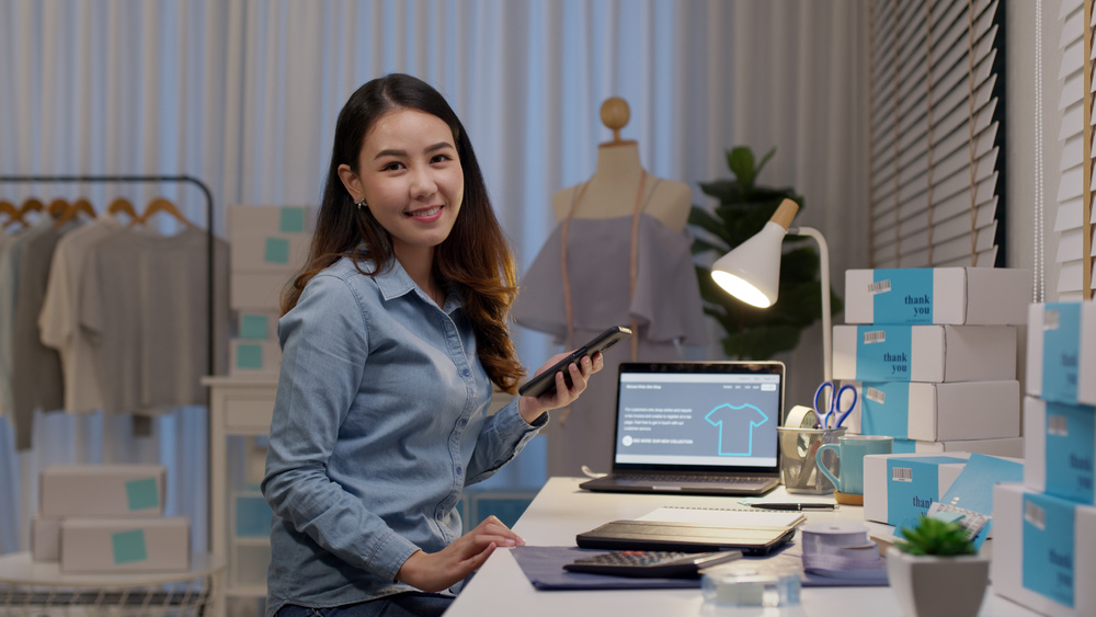 A young woman entrepreneur sorting out parcel delivery at her laptop in her home.